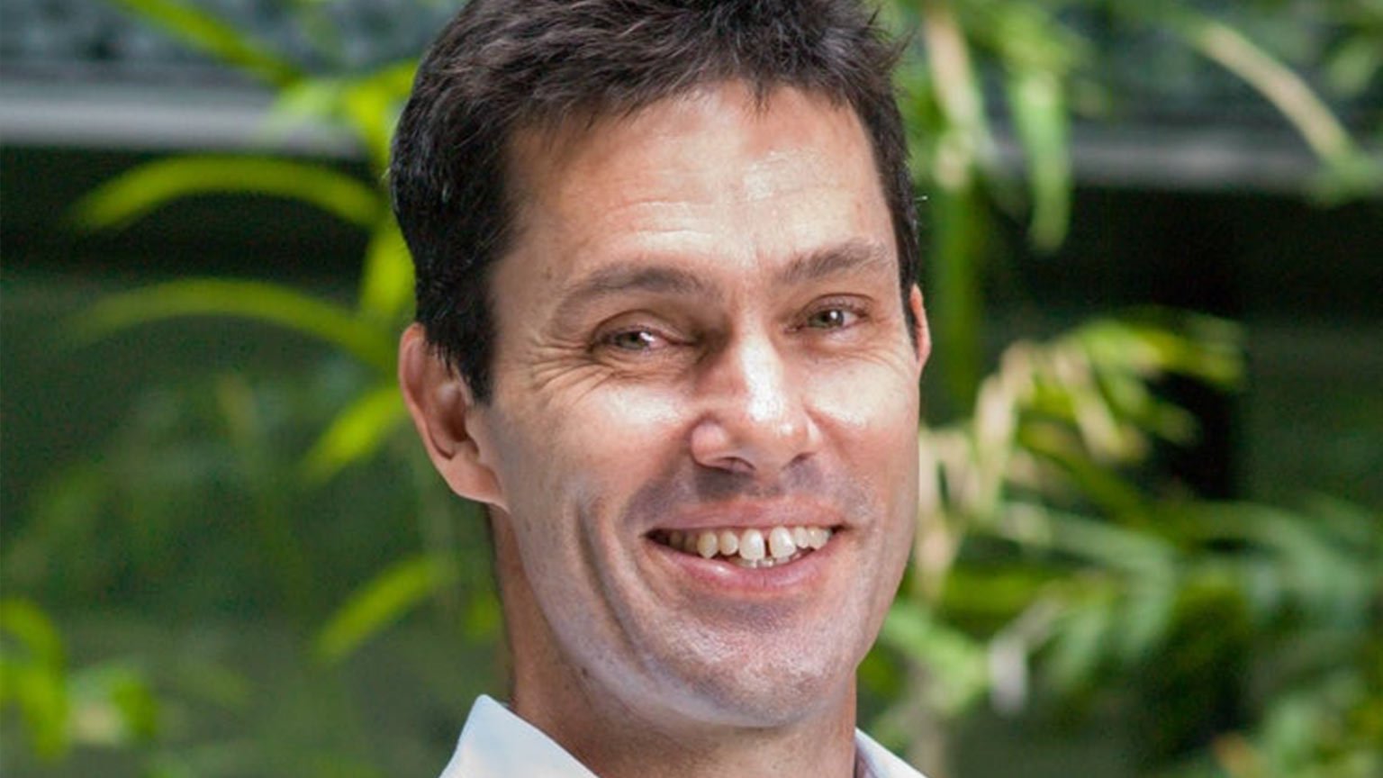 Man smiling standing in front of green plants.
